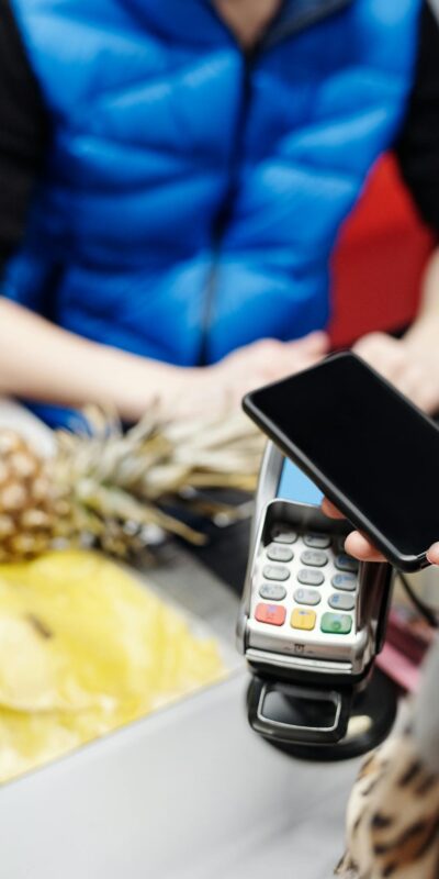 A customer uses a smartphone for contactless payment at a retail checkout with fresh produce.