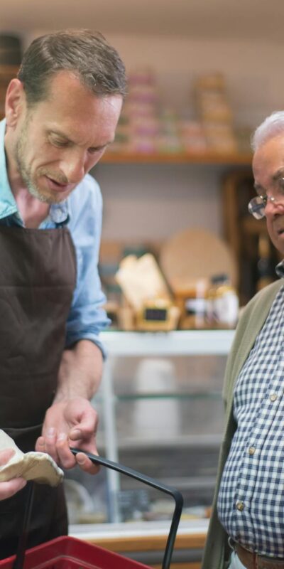 Friendly grocery store interaction between a salesman and senior customer in Portugal.