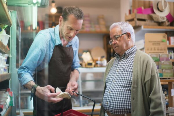 Friendly grocery store interaction between a salesman and senior customer in Portugal.