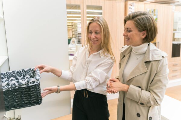 Two women smiling as they examine a decorative basket in a home goods store.